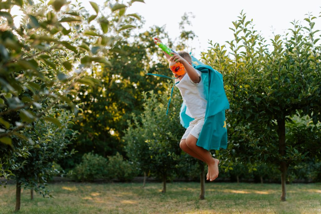 boy in super hero costume leaping over grass