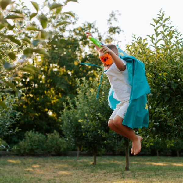 boy in super hero costume leaping over grass